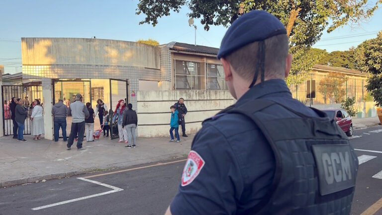 Fotografia mostra agente da Guarda Municipal de Londrina em frente a uma escola, durante entrada e saída de alunos.